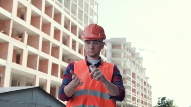 Ritratto in vita di un costruttore concentrato che spruzza disinfettante nel palmo della mano mentre si trova tra nuovi edifici incompiuti. Rallentatore - Filmati, video