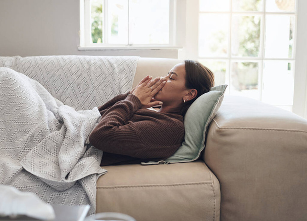 Хвора жінка, чхає і дме ніс з хворобою, грипом або холодним на дивані у вітальні вдома. Молода жінка з тканиною для бактерій, лихоманки або грипу втомлюється або відпочиває на кушетці вдома. - Фото, зображення