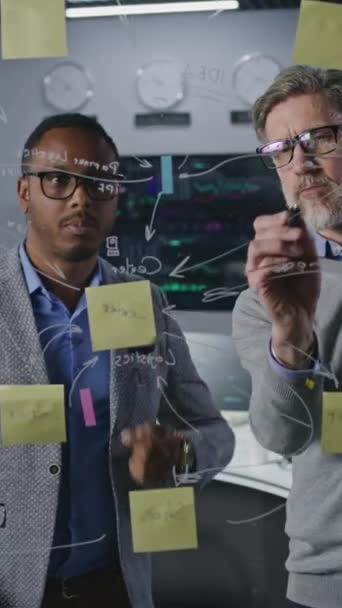 多人種金融アナリストは、投資銀行のオフィスでガラス壁に描画し、会社の暗号ビジネス戦略を開発して分析します。コンピュータと背景にリアルタイム株式を持つ大きなデジタル画面 - 映像、動画
