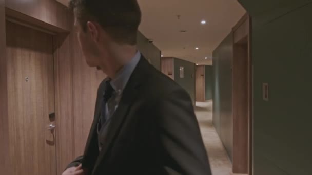 ホテルの廊下の部屋を歩いている警備員. ストッククリップ。 暗い建物のホールでスーツを着た若者  - 映像、動画