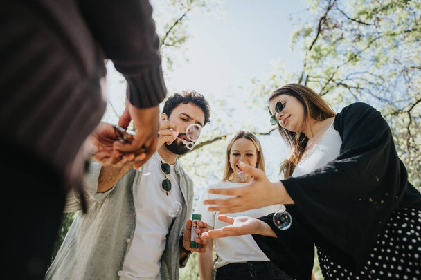 A group of multiracial friends share joyful moments outdoors, blowing bubbles and laughing. A sunny, urban park setting enhances the carefree and relaxing atmosphere. - Photo, Image
