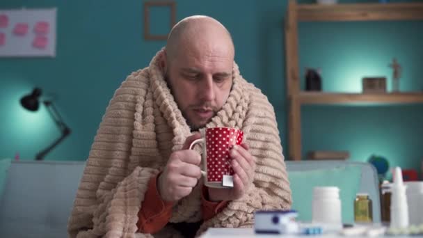 Nemocný muž s bolestí hlavy, sezónními infekcemi, chřipkou sedící na gauči a pijící čaj. Nemocný muž přikryl pokrývku vysokou horečkou a doma měl chřipku. Kopírovat prostor - Záběry, video