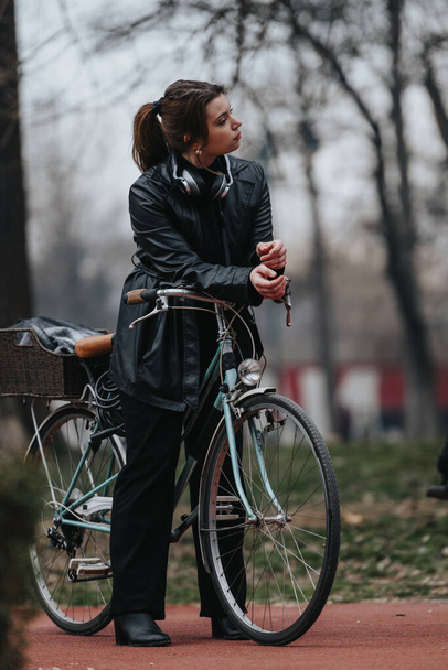 Una giovane donna elegante e sicura di sé in abito da lavoro in piedi con la sua bici vintage in un parco sereno. - Foto, immagini