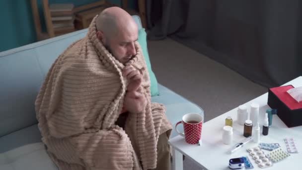 Een bebaarde zieke man met koorts bedekt met een deken op de bank. Griepconcept - Video