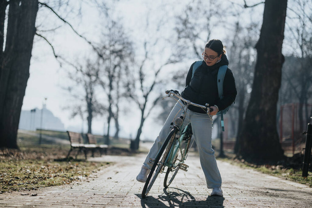 A woman with a bicycle takes a break in a serene park. The scene captures the tranquility of a solo outdoor activity on a clear day. - Photo, Image