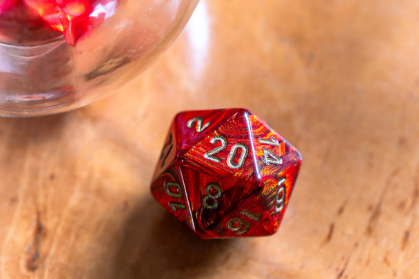 Close-up of a vibrant red D20 die, emphasizing its detailed markings on a warm wooden background, perfect for gaming and fantasy themes. - Photo, Image