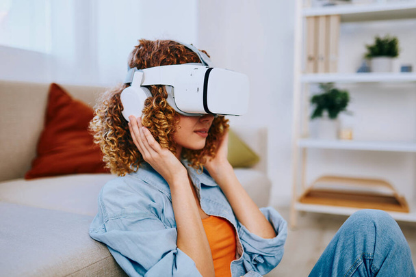 Donna sorridente che si gode il gioco della realtà virtuale a casa con occhiali VR futuristici sul divano - Foto, immagini
