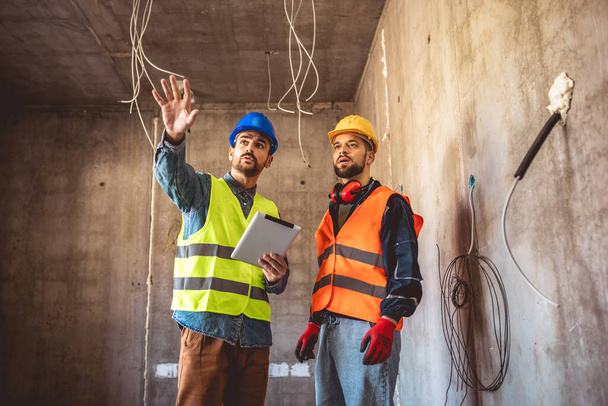 Dos trabajadores de la construcción trabajando juntos en la obra. Visitar nuevos edificios y planificar nuevos trabajos. - Foto, imagen