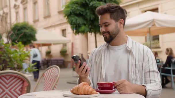 Başarılı bir beyaz adam cep telefonuyla konuşuyor yakışıklı işadamı arıyor kahvaltı yapıyor kahve içiyor kruvasan kafe restoranı, şehrin dışında finans merkezi işvereni sohbeti yapıyor. - Video, Çekim