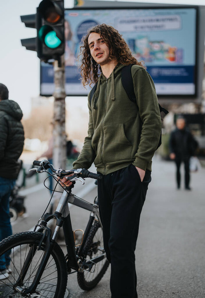 Ein junger Mann steht mit seinem Fahrrad im Freien und strahlt eine entspannte Atmosphäre aus, während er die städtische Umgebung um sich herum genießt.. - Foto, Bild