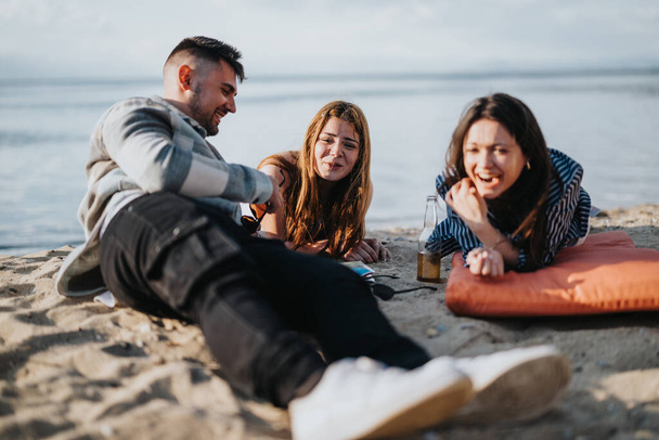 Una alegre escena de playa con tres amigos riendo y disfrutando de la compañía de los demás, capturando la esencia de la felicidad y el ocio junto al mar. - Foto, imagen