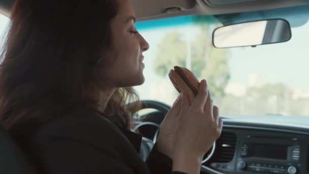 Porträt einer Frau, die im Auto sitzt, leckeres Sandwich in der Hand hält und es riecht, isst. Zeitlupenvideo - Filmmaterial, Video