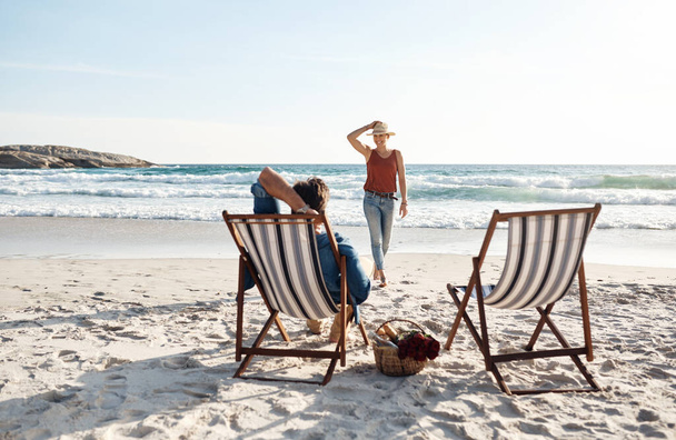 Couple, love and relax on chair at beach for picnic, relationship and walking on sand in nature. Man, woman and romance in summer for vacation, holiday and anniversary on tropical island for date. - Photo, Image