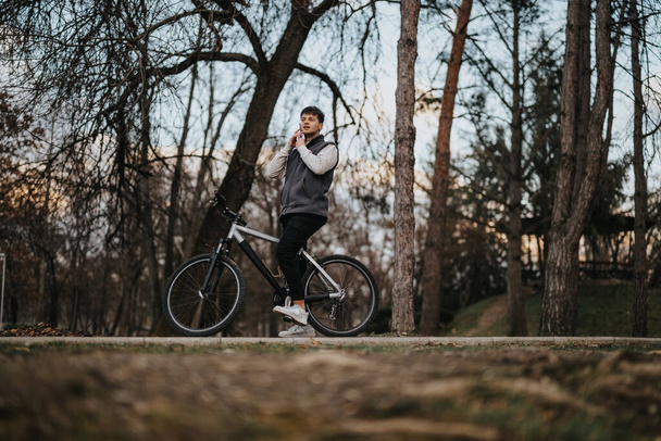 Młody nastolatek na rowerze robi sobie przerwę na wypoczynek w spokojnej scenerii jesiennego parku. - Zdjęcie, obraz