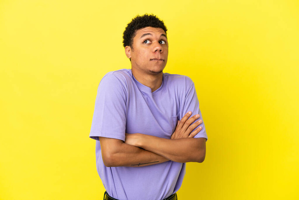 Mladý africký Američan izolovaný na žlutém pozadí dělat pochybnosti gesto při zvedání ramen - Fotografie, Obrázek
