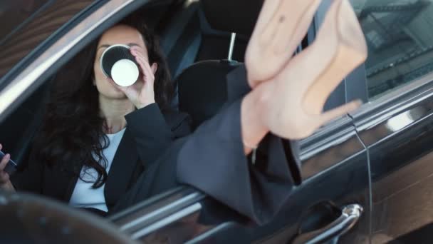 Dame op hakken open autoraam, zitten en ontspannen in de auto, typen op smartphone, drinkt koffie. Video in slow motion - Video