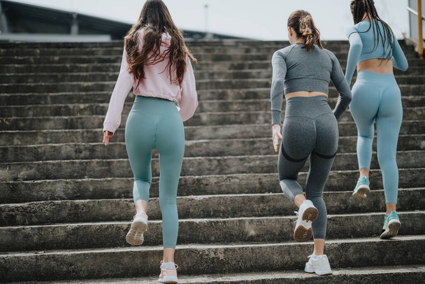 トレーニングギアの3人の運動女性が階段を歩き,決意とフィットネスを象徴する. - 写真・画像