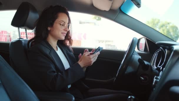 Portret van een vrolijke vrouw in een auto met open raam, ontspannen, typen op smartphone en lachen. Video in slow motion - Video