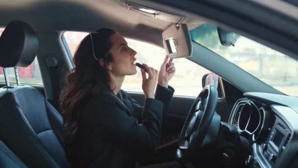 Portret van een vrouw die in de auto zit, naar de spiegel kijkt, lippenstift vasthoudt en make-up maakt. Video in slow motion - Video