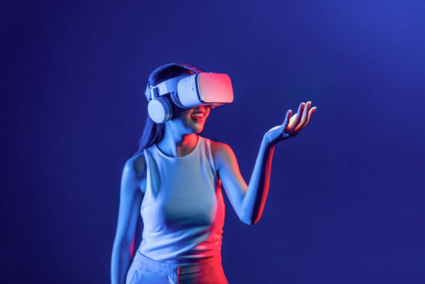 Smart Female de pie rodeada de auriculares VR de neón que conectan tecnología de comunidad ciberespacial metaversa y futurista. Mujer elegante uso de la celebración de la mano generado objeto virtual. Alucinaciones. - Foto, Imagen