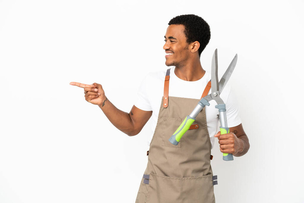 アフリカ系アメリカ人庭師男性は,孤立した白い背景の上にシアを傾け,指を横に指し,製品を提示しています - 写真・画像