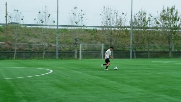 Teenage fotbalista běží s míčem podél fotbalového hřiště. - Záběry, video