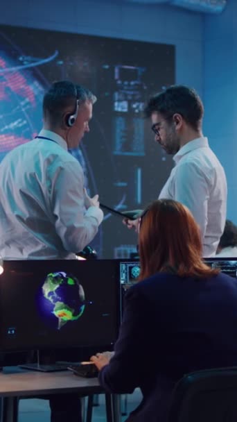 Tiro vertical de homens discutindo dados em tablet e tela grande enquanto trabalhava no problema do aquecimento global no centro de controle de ecologia - Filmagem, Vídeo