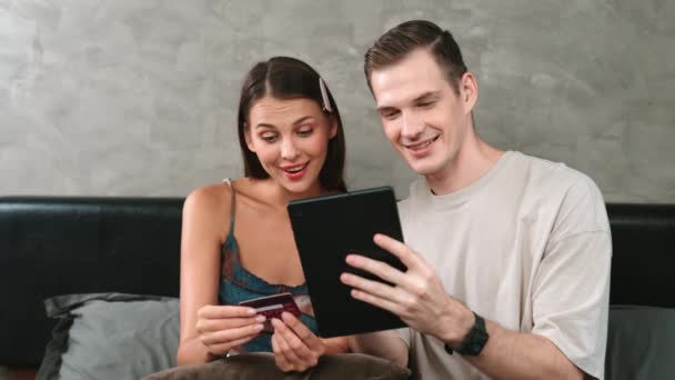 Νεαρό ζευγάρι κάθεται στο υπνοδωμάτιο σπίτι χρησιμοποιώντας online εφαρμογή πληρωμής και ψηφιακό πορτοφόλι στο tablet για να πληρώσει με πιστωτική κάρτα. Αγορές ηλεκτρονικού εμπορίου και σύγχρονες αγορές μέσω mobile internet. Διεύθυνση - Πλάνα, βίντεο