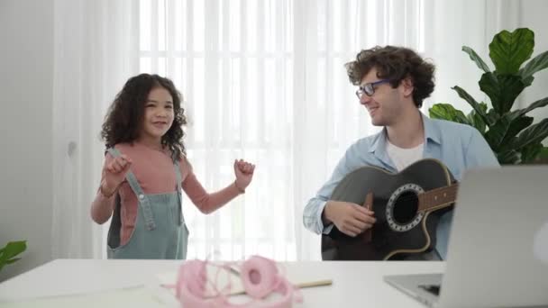Çekici beyaz bir baba gitar çalarken tatlı bir kız müzik eşliğinde dans ediyor. Mutlu baba ve Amerikalı kız birlikte vakit geçirirken akıllı çocuk müzik yapıyor. Aile eğlence konsepti. Pedagoji. - Video, Çekim
