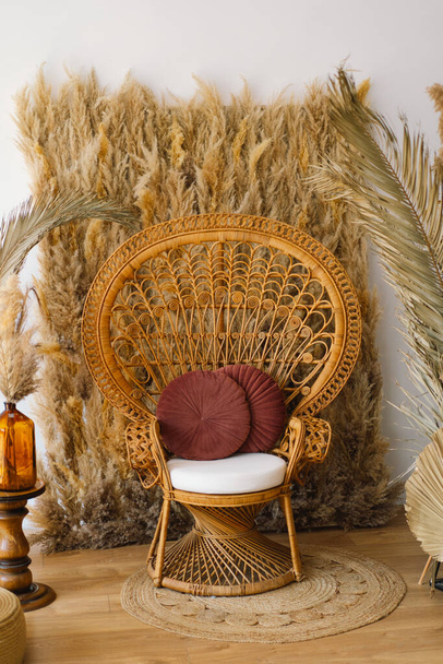 Een gezellige hoek is voorzien van een vintage geïnspireerde rotan pauw stoel versierd met een zacht wit kussen en een Bourgogne gooien kussen. - Foto, afbeelding