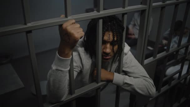 Naštvaný americký teenager stojí ve vězení ve vězeňské cele a drží kovové mříže. Mladí vězni hrají karty na posteli v pozadí. Středisko pro zadržování mládeže nebo nápravné zařízení. Vysoký úhel. - Záběry, video