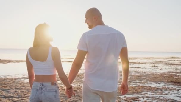 Joven sonriente abrazando a su novia contra la puesta de sol cerca del mar. Concepto romántico de relación. Movimiento lento - Imágenes, Vídeo