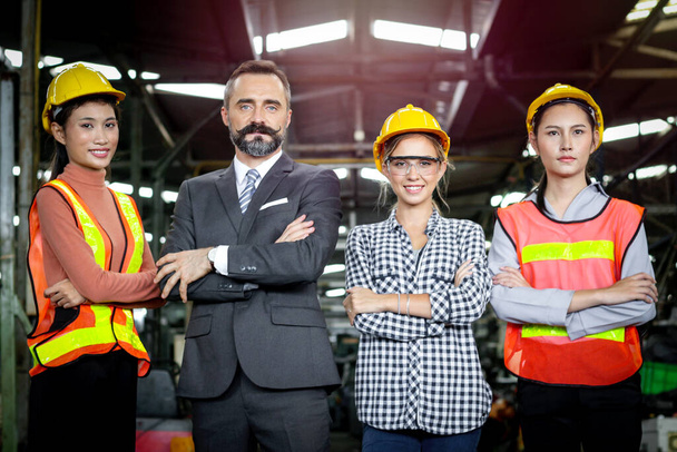 Senior businessman manager with industrial engineer women with safety helmet stand in line at manufacturing industry factory. Group of industrial workers and boss stand with arms crossed at workplace. - Photo, Image