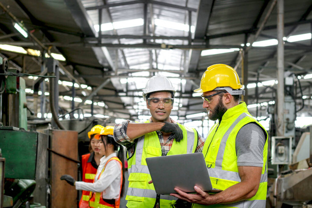 Industrial foreman and worker with helmet and safety vest using laptop computer during discussing together at manufacturing industry factory. Engineer inspecting workplace and checking process. - Photo, Image