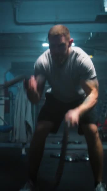 Αρσενικές ασκήσεις αθλητή με σχοινιά μάχης σε σκοτεινό γυμναστήριο πυγμαχίας με φωτισμό LED. Επαγγελματίας πυγμάχος κάνει καρδιο ή προπόνηση αντοχής πριν από τον αγώνα πρωτάθλημα. Κάθετη βολή - Πλάνα, βίντεο