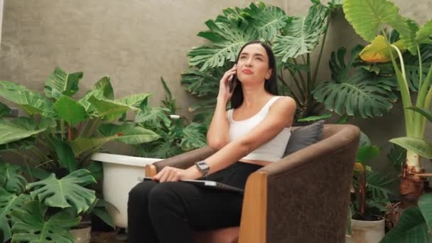 Modern genç kadın telefonda konuşuyor, uzaktan çalışıyor ya da tropik bitkilerle birlikte minimalist bir mimari beton stil yaz egzotik bitki yetiştirme bahçesinde yalnız başına dinleniyor. Blithe - Video, Çekim
