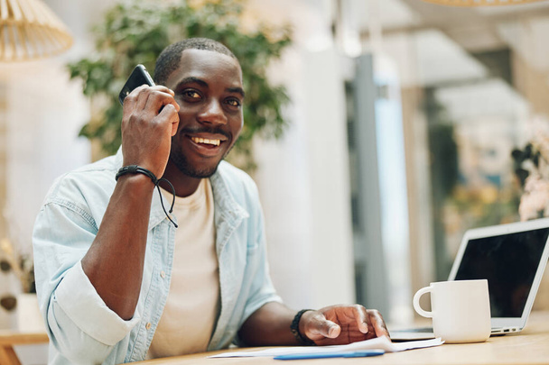 Styl życia człowiek Afryki szczęśliwy portret profesjonalista mężczyzna biznes praca patrząc telefon dorosły biznesmen biuro siedzi młody komputer czarny uśmiechnięta technologia - Zdjęcie, obraz