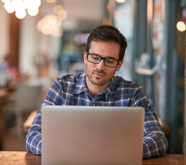 Ελεύθερος επαγγελματίας, laptop και άνθρωπος με γυαλιά στο εστιατόριο για online έρευνα, απομακρυσμένη εργασία και δικτύωση για εργασία. Άντρας, blogger και υπολογιστής σε καφετέρια για κοινωνικά δίκτυα, ενημερώσεις και καριέρα. - Φωτογραφία, εικόνα