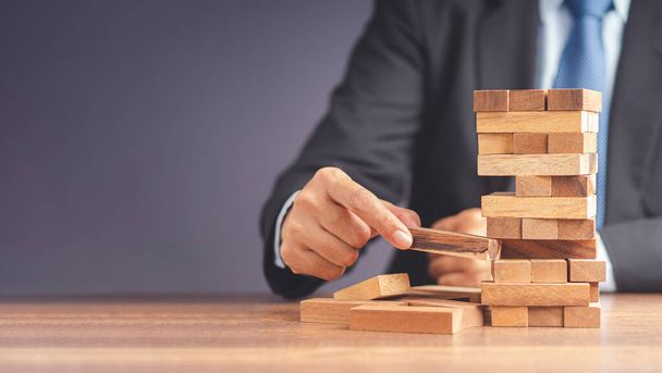 Risk of management and strategy plans for business growth and success concept. Close-up hand of the businessman in a suit playing a wooden block game while sitting at the work table. Space for text - Photo, Image