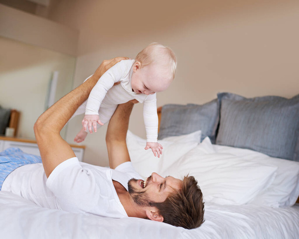 Αγάπη, χαμόγελο και το μωρό με τον πατέρα στο κρεβάτι χαλαρώνοντας, παίζοντας και δένοντας μαζί στο σπίτι. Ευτυχισμένος, γλυκός και νεαρός μπαμπάς ξαπλωμένος με κορίτσι, βρέφος ή παιδί σε υπνοδωμάτιο ή παιδικό δωμάτιο στο σπίτι της οικογένειας - Φωτογραφία, εικόνα