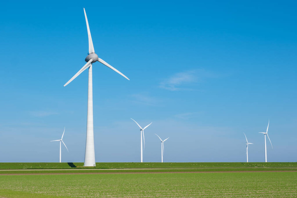 Joukko tuuliturbiineja pyörii kauniisti laajalla vihreällä pellolla valjastaen tuulen voiman tuottamaan puhdasta energiaa Alankomaille.. - Valokuva, kuva