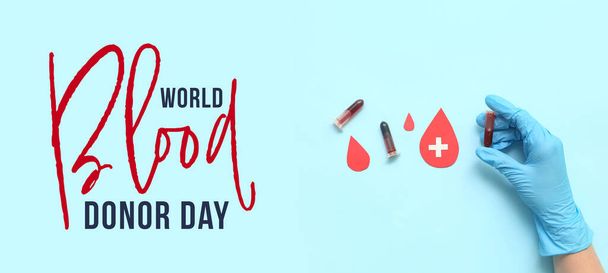 Banner για την Παγκόσμια Ημέρα αιμοδοσίας με το χέρι στο γάντι κρατώντας δοκιμαστικό σωλήνα και σταγόνες αίματος από χαρτί - Φωτογραφία, εικόνα