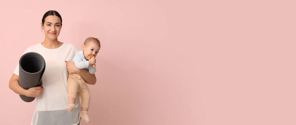 Young sporty woman with yoga mat holding her baby on pink background with space for text - Photo, Image