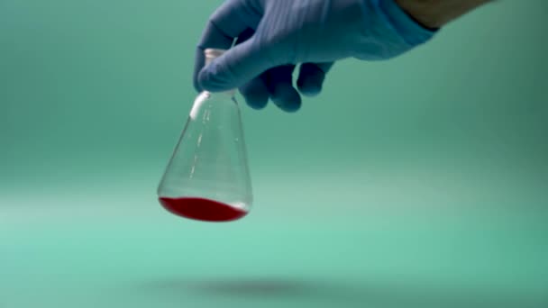 Mão de médico anônimo em luva de látex segurando frasco cônico com amostra química vermelha em laboratório durante o teste de diagnóstico - Filmagem, Vídeo