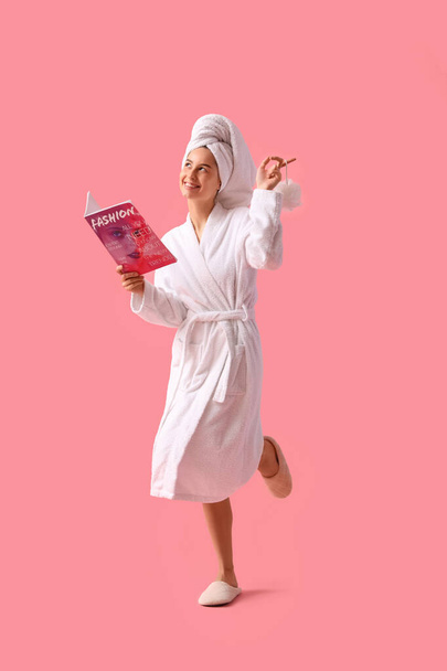 Jeune femme en peignoir avec magazine et loofah après la douche sur fond rose - Photo, image