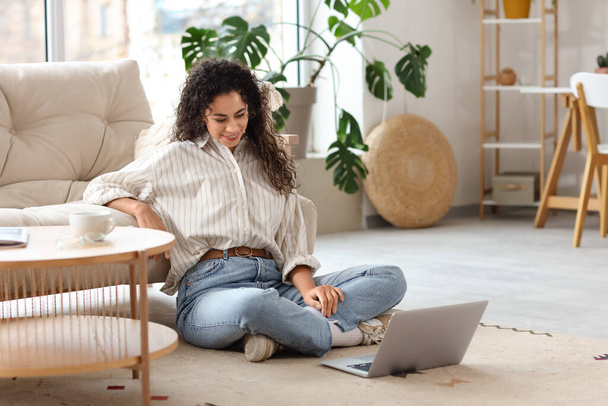 Joven mujer afroamericana con el ordenador portátil de chat de vídeo en el suelo en casa - Foto, Imagen