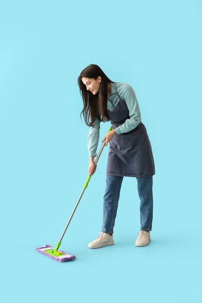 Jeune femme en tablier sol de nettoyage sur fond bleu - Photo, image
