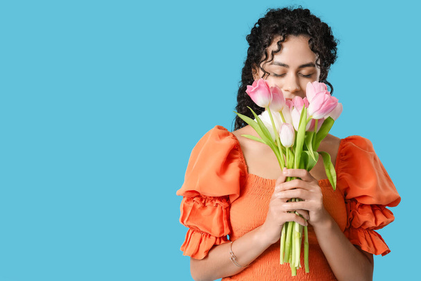Piękna młoda Afroamerykanka z bukietem tulipanów na niebieskim tle. Międzynarodowy Dzień Kobiet - Zdjęcie, obraz