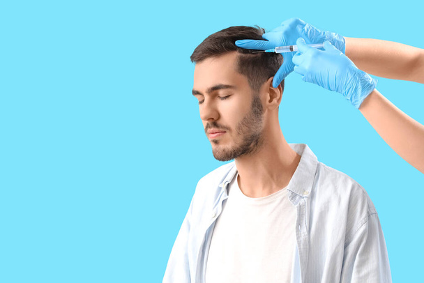 Young brunette man receiving injection for hair growth on blue background, closeup - Photo, Image