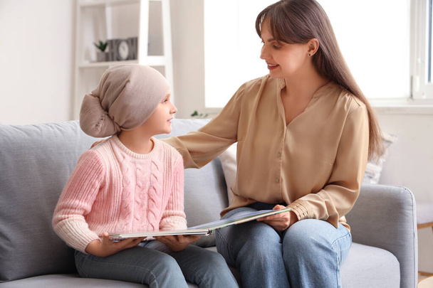 Κοριτσάκι μετά τη χημειοθεραπεία με τη μητέρα της να διαβάζει βιβλία στο σπίτι. Διεθνής Ημέρα κατά του καρκίνου της παιδικής ηλικίας - Φωτογραφία, εικόνα